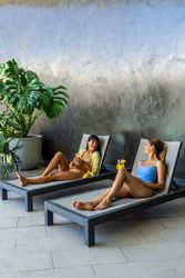 Two women friends are resting on lounge chairs, one of them holding a drink. The scene is relaxed and casual