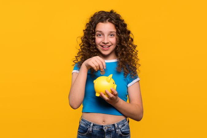 Girl smiling while putting coin into a piggy bank
