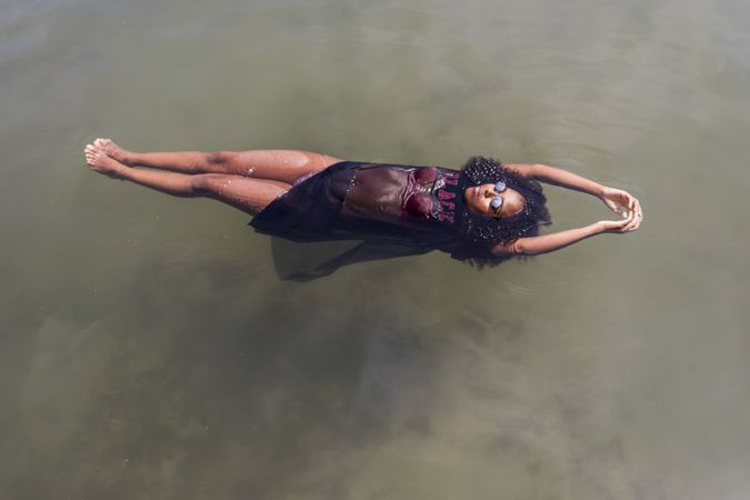 Beautiful young Black woman floating in a pool of water on sunny day