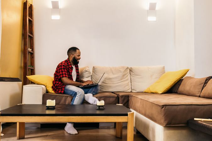 Black man in casual clothes using laptop at home.