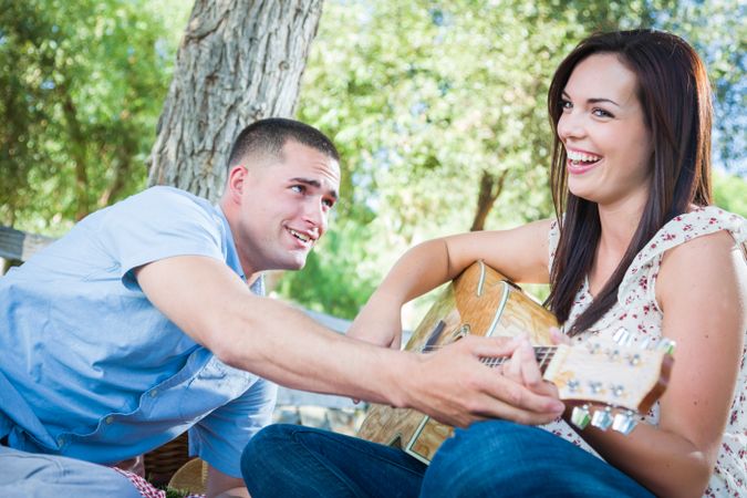 Young Adult Man Teaching Girlfriend How To Play The Guitar Outside in the Park.
