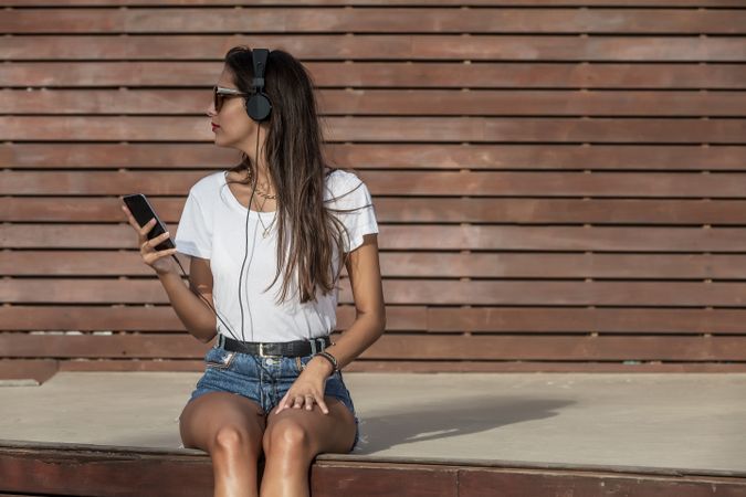 Woman using headphone to listen to music sitting on a bench looking away