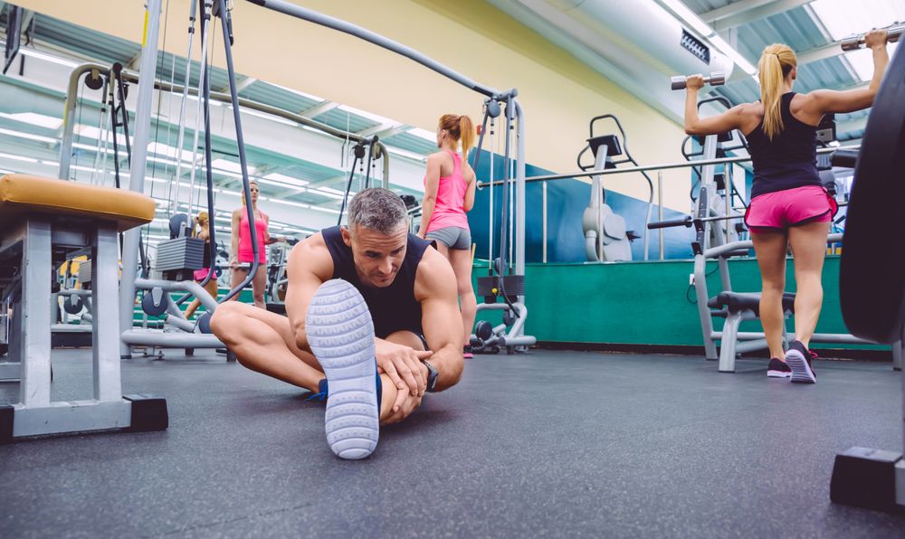Male stretching on floor of busy gym
