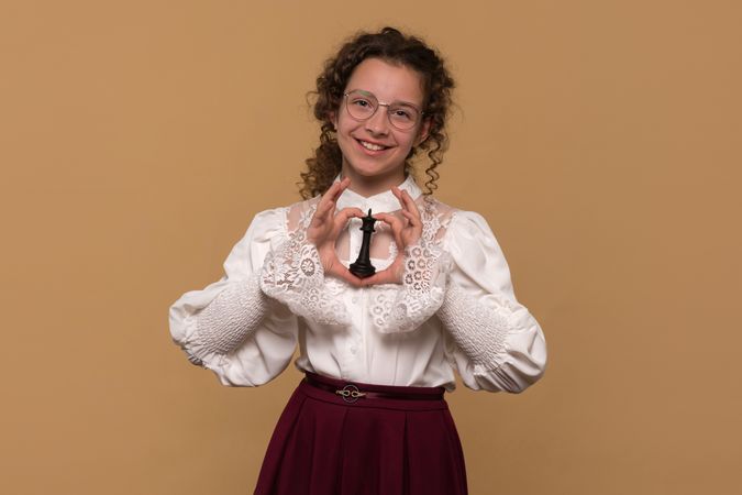 Young girl with glasses confidently smiling while displaying black chess piece.