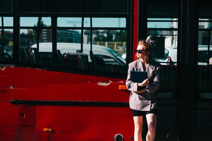 Woman with tablet in stylish suit standing nearby red bus