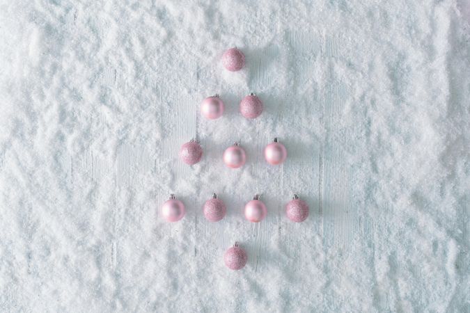 Wooden table background with snow and festive pink baubles in the shape of a tree