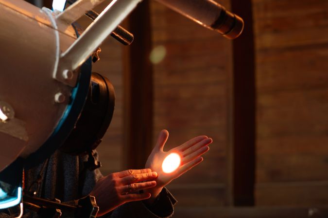 Man observes glowing spot of telescope light on hand.