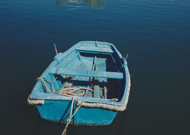 Small empty blue boat moored and floating in sea