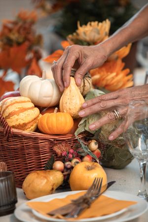 Cropped image of hands taking small pumpkin from a wicker basket on dinner table