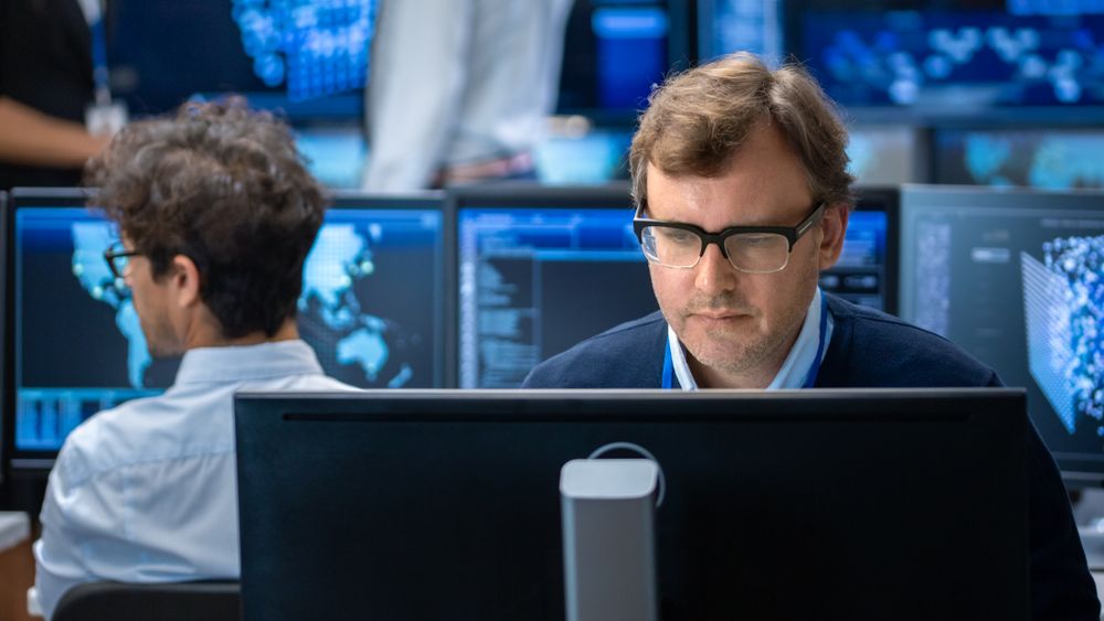 Neural Network Algorithm Architect Working at His Workstation in a Busy Creative Office.