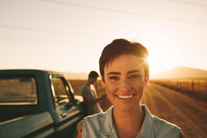 Close up of smiling woman standing on dirt road with partner in background