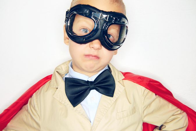 Blond boy wearing airplane goggles and cape with his hands on hips
