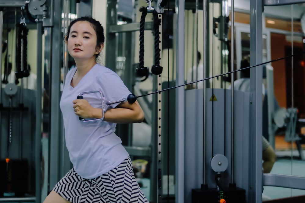 A woman is actively exercising on a cable machine inside a fitness center