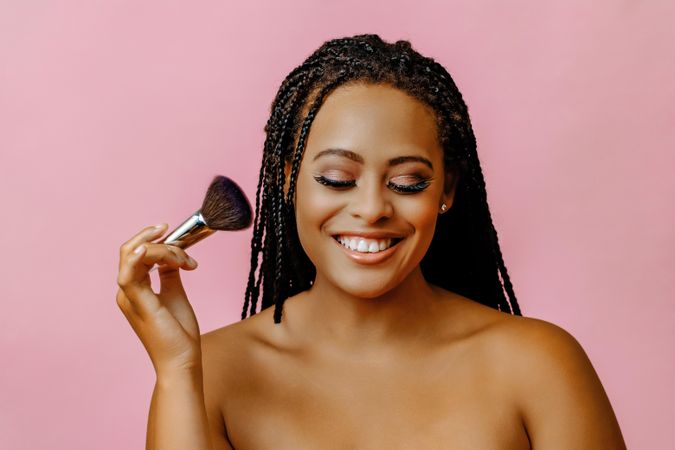 Smiling Black woman holding make up brush to her cheek with eyes closed