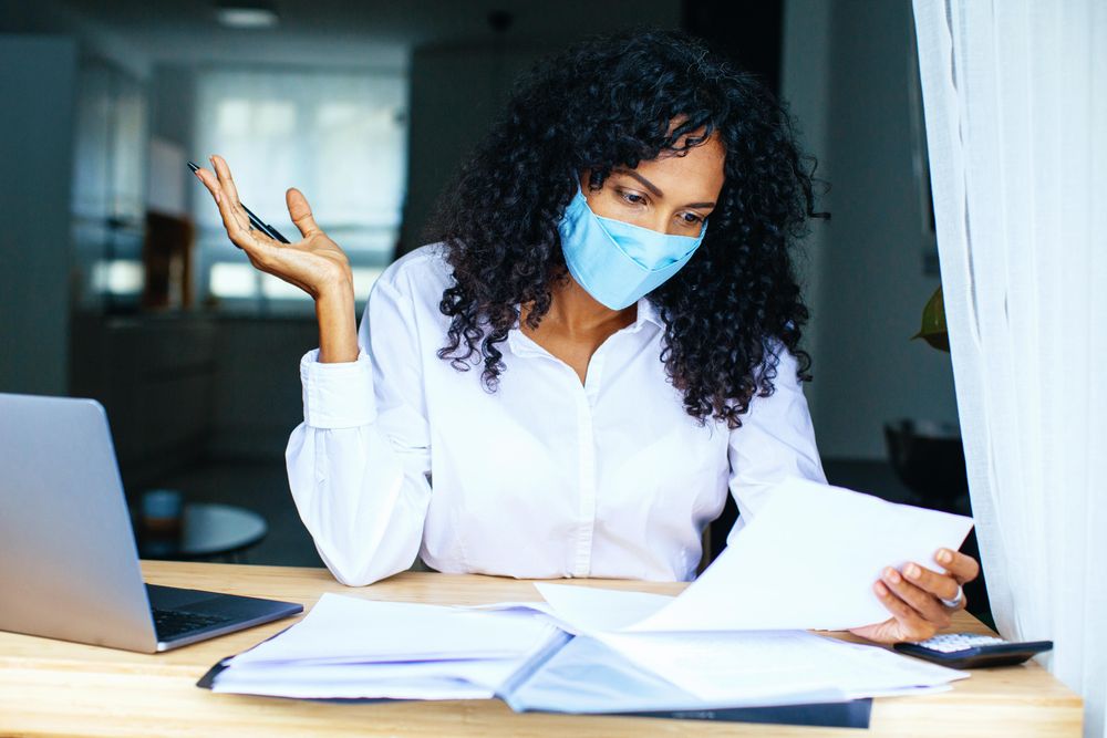 Woman frustrated while reading over documents with a laptop while wearing a facemask