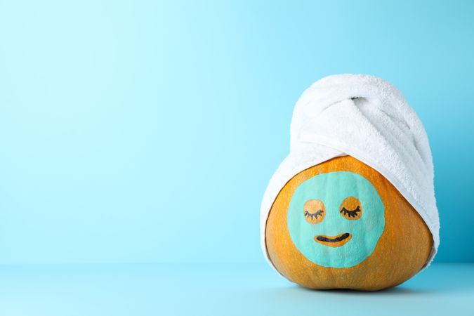 Pumpkin with facial mask and towel on blue background, copy space