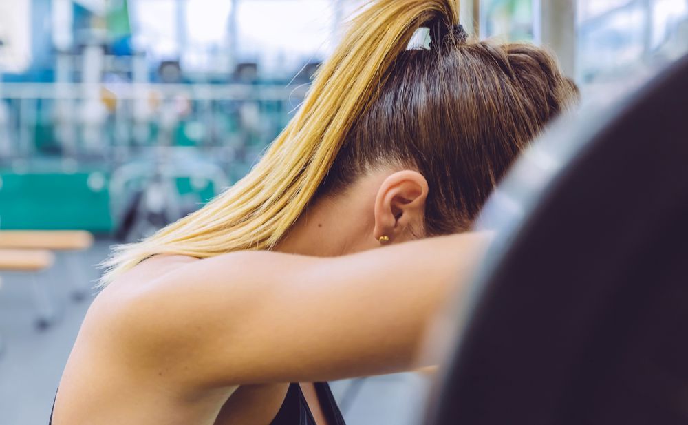 Woman resting head on barbell between tough sets