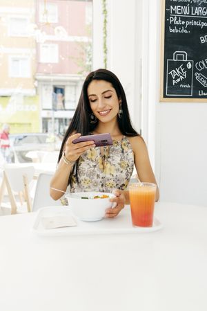 Cheerful woman with healthy food taking photo in cafe