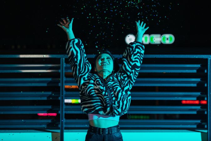 Trendy Asian woman in a stylish  coat throwing confetti on a roof