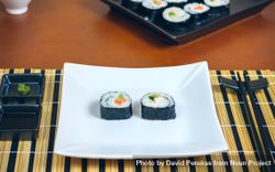 Two freshly made sushi rolls on rectangular plate on mat, ready to eat 5rdXMb