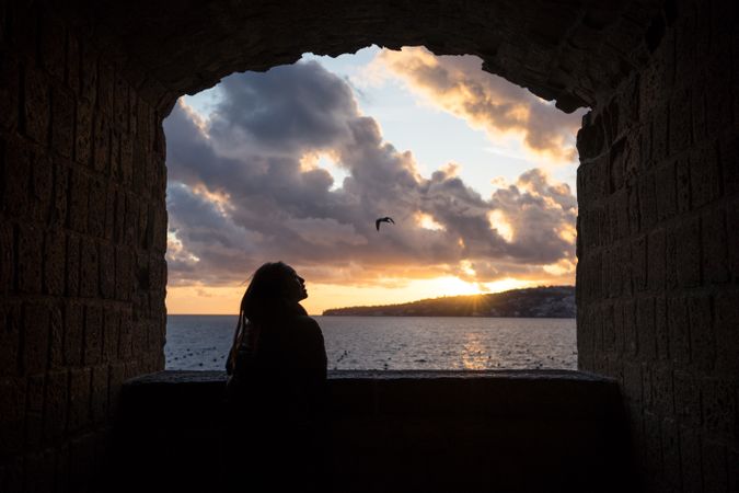 Joyful female on vacation in warm wear delighting in sunset on seashore