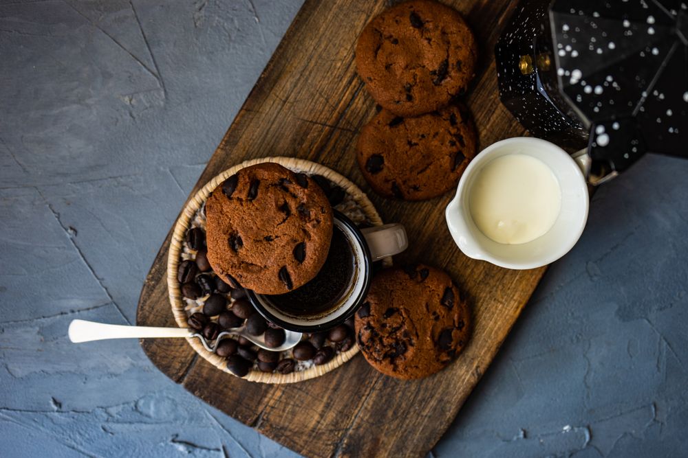Top view of coffee surrounded by cookies and chocolate