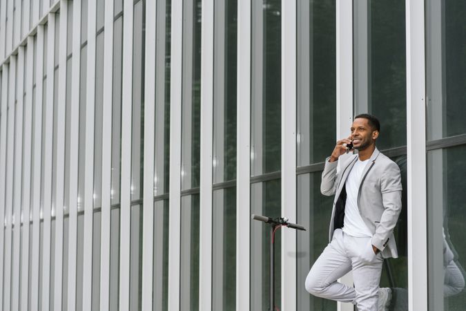 Elegant Black man talking smartphone leaning building
