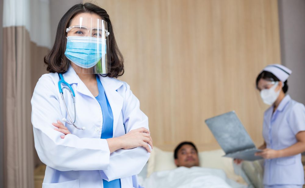 Asian female doctor wearing medical protective face shield and mask with arms crossed