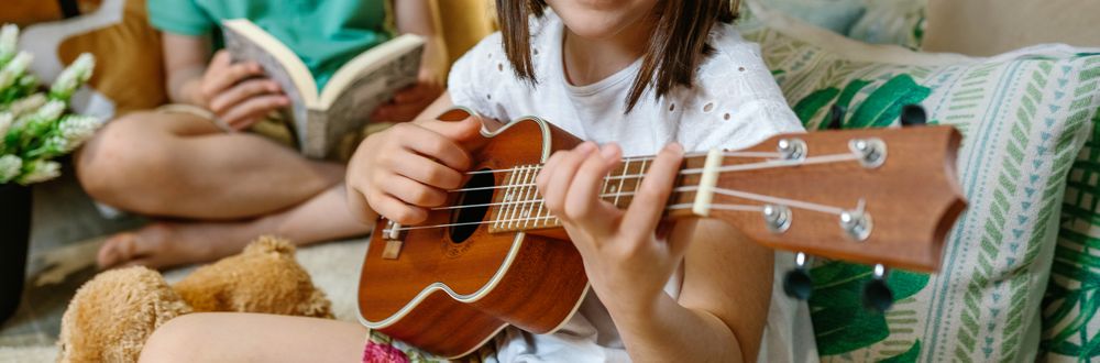 Banner of unrecognizable little girl playing ukulele while boy reading book on handmade shelter tent