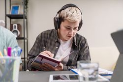Young creative focused on handwritten notes while listening to music at workspace