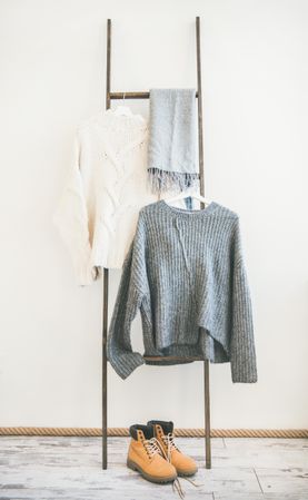 Woolen sweaters, grey scarf and winter boots on modern garment rack