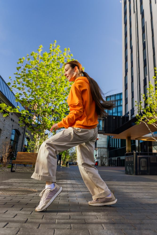 Vertical Screen: Young And Stylish Female Hip-Hop Dancer Freestyling On City Street Among Modern Buildings. Street Style Performer Doing Improvisation.