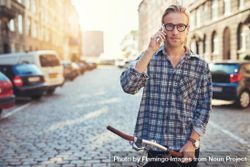Man in glasses on his cellphone on a European cobble street with bicycle bxgeB4
