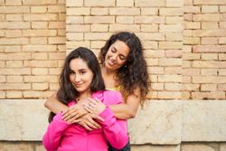 two young women friends embrace each other smiling with joy