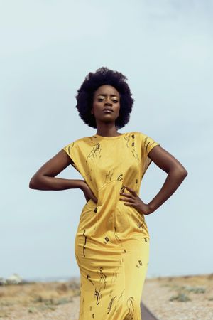 Black woman posing in yellow dress under blue sky
