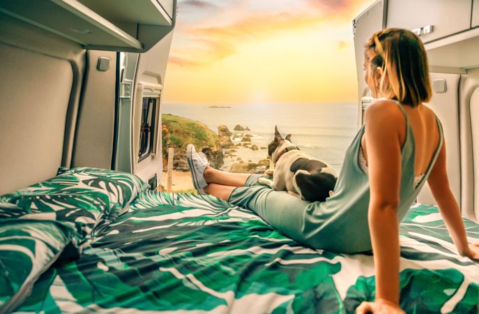 Female sitting in motorhome bed with cute dog enjoying coastal view