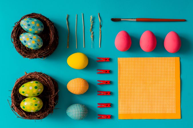 Bright Easter eggs, birds nests and clothes pins on cyan paper