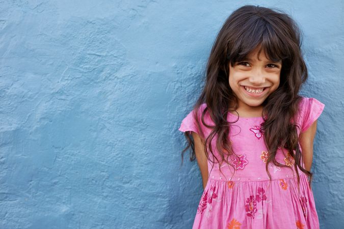 Portrait of cute little girl looking at camera and smiling standing against blue wall
