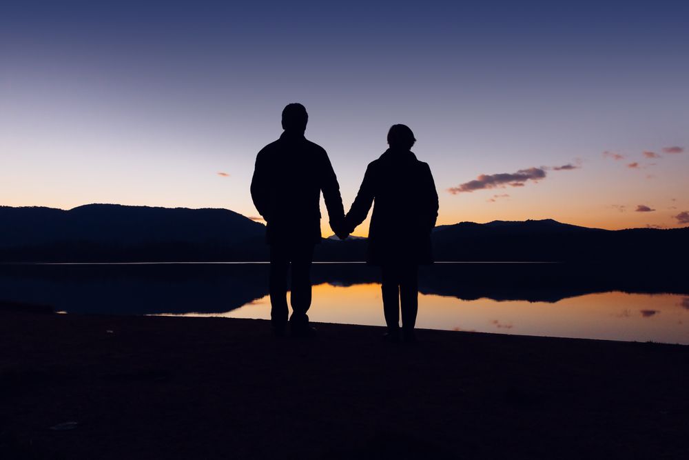Anonymous couple standing near water during sunset