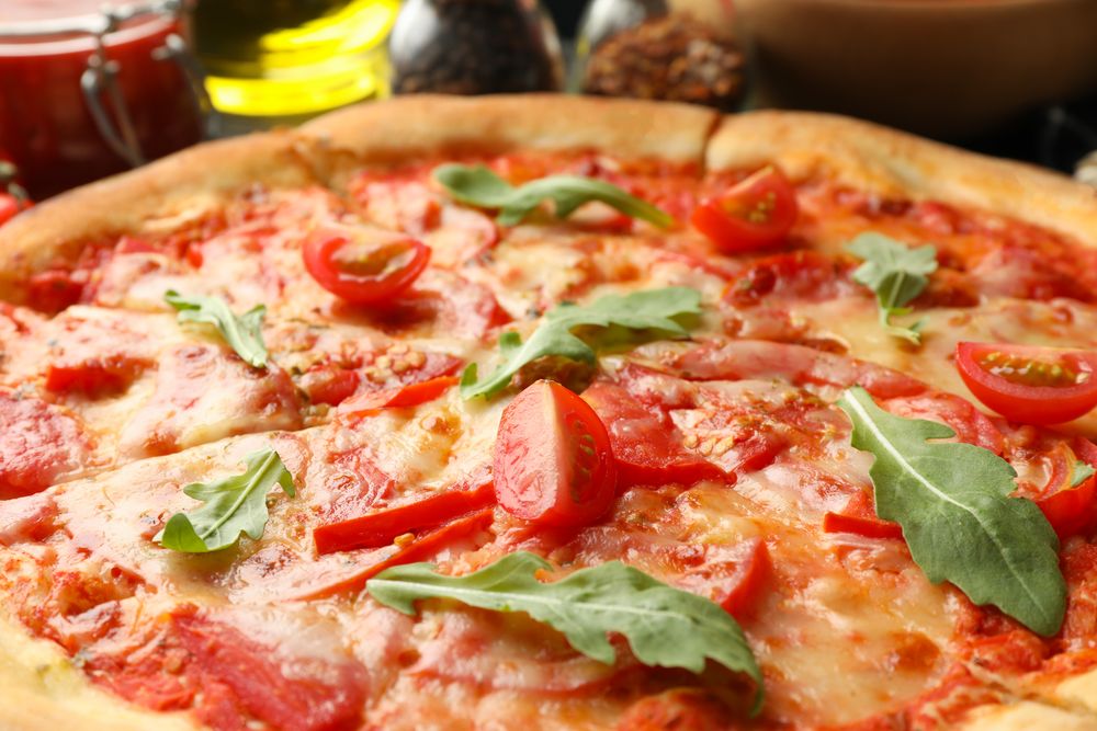 Tasty pizza with tomatoes and arugula leaves, close up