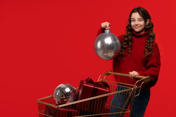 Smiling girl in red sweater holds large silver Christmas ornament